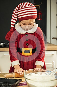 Cute girl making dough for Christmas cookies. Little kid wearing Christmas outfit and having fun while cooking in the kitchen.