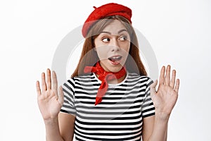 Cute girl mime wearing red beret and striped t-shirt, raising hands as if leaning on invisible wall, making performace