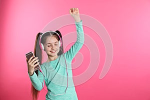 Cute girl with mobile phone enjoying music in headphones on color background