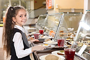 Cute girl near serving line with healthy food in canteen