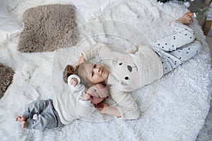 Cute girl with a newborn baby brother relaxing together on a white bed