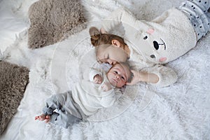 Cute girl with a newborn baby brother relaxing together on a white bed