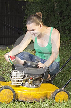 Cute girl oiling and repairing yellow lawn mower