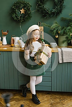 Cute girl opens a Christmas or new year gift in the interior of the emerald kitchen