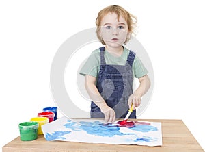 Cute girl painting on small desk looking to camera