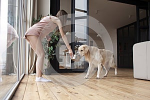 cute girl in pajamas gives food to dog in a bowl, woman feeds pet at home, hungry golden retriever is waiting for food