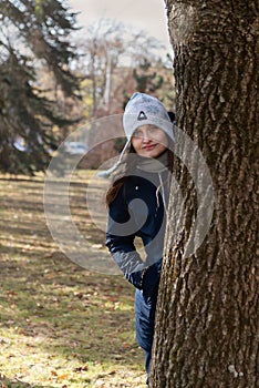 Cute girl peeks out from behind tree