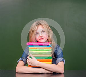 Cute girl with pile books near empty green chalkboard