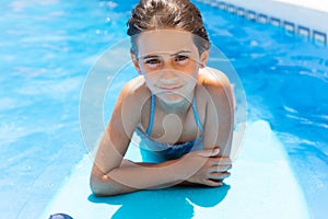 Cute girl playing with a bodyboard in a swimming pool.