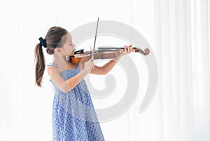 Cute girl playing violin in white bedroom with white curtain background. Musical and people lifestyles. Education and recreation