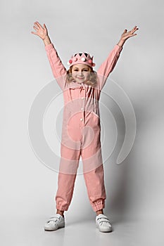 cute girl with a plush crown, stands in full growth with her hands up. in a cotton summer jumpsuit, dusty rose color