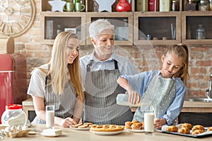 Cute girl pouring milk to granny and mom at kitchen