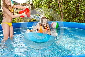 Cute girl pouring water over her friend in pool