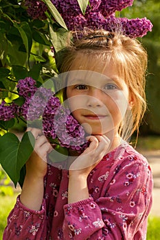 Cute girl in purple dress posing with lilac flowers. Portrait of little girl with lilac, spring mood.