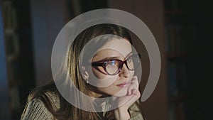 Cute girl putting on glasses and thinking at the desk in half-light library