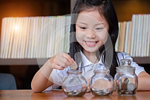 Cute girl putting money coins in glass,saving money concept