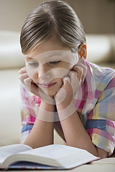 Cute girl reading book while lying at home