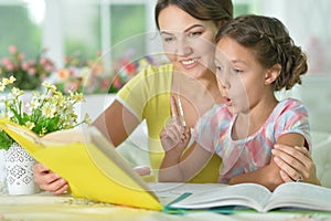 Cute girl reading book with mother at the table at home