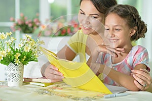 Cute girl reading book with mother at the table at home