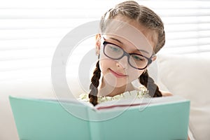 Cute girl reading book near window at home