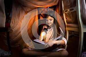 Cute girl reading book in self-made house with flashlight