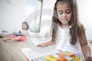 Cute girl reading book with sister in background at home
