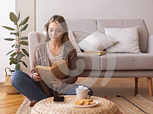 Cute girl reading book, sitting on floor at home, empty space
