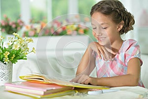 Cute girl reading book at the table at home