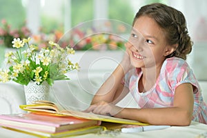 Cute girl reading book at the table at home