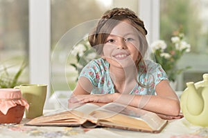 Cute girl reading book at the table at home