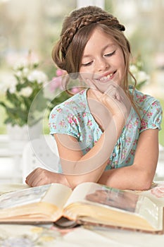 Cute girl reading book at the table at home