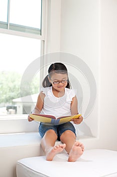 Cute girl reading book on window