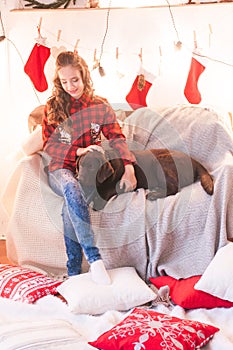 Cute girl in a red checkered shirt with dog labrador at home in the room decorated for Christmas.