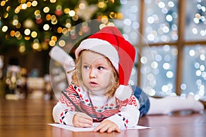 Cute girl in red christmas hat writes letter to Santa Claus