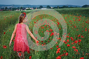 Cute girl in red dress walks at poppy field