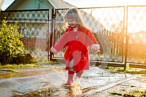 Cute girl in a red jacket is jumping in the puddle.The setting warm summer or autumn sun. summer in the village