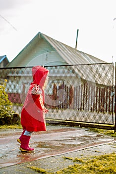 Cute girl in red jacket is jumping in puddle.The setting warm summer or autumn sun. summer in village
