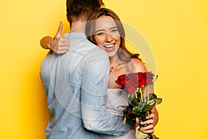 Cute girl with red roses showing a thumb while hugging her boyfriend.