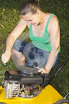 Cute girl repairing yellow lawn mower