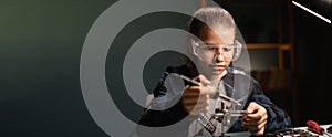 Cute girl in safety glasses, learning how to solder microprocessor cables and printed circuits uses a magnifying glass