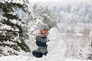 Cute girl sculpts snowman in winter day. photo