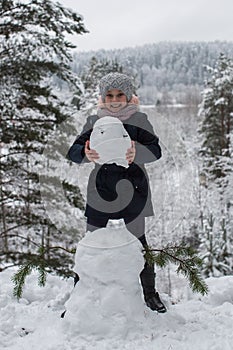 Cute girl sculpts snowman in winter snowy Park.