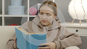 A cute girl is sitting on the couch and reading a fascinating book.