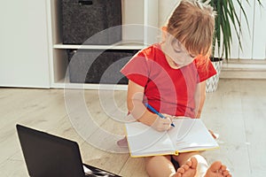 Cute girl is sitting on the floor with a laptop, a pen and a notepad.