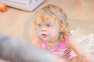 Cute girl sitting on the kitchen floor soiled with flour, playing with food, making mess and ha photo