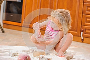 Cute girl sitting on the kitchen floor soiled with flour, playing with food, making mess and ha photo
