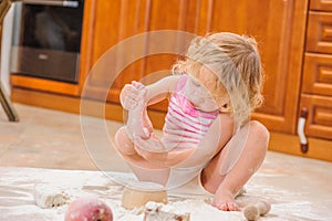 Cute girl sitting on the kitchen floor soiled with flour, playing with food, making mess and ha