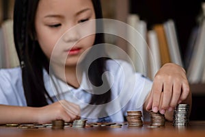 Cute girl sitting in library putting money coin to stack on table,saving money concept