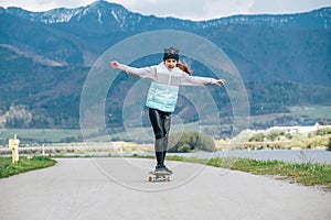 Cute girl skateboarding on the longboard on the asphalt road with a mountain landscape background. She gracefully balancing when