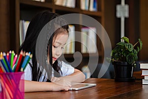 Cute girl smile sitdown and playing tablet smartphone in the lib